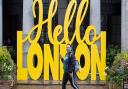 A woman wearing a face mask passes a 'Hello London' sign in Covent Garden, London, following the further easing of lockdown restrictions in England