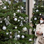 A woman wearing a face mask walks passes a display of Christmas trees outside a shop in central London