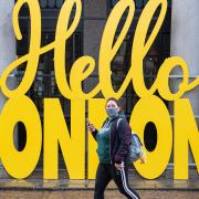 A woman wearing a face mask passes a 'Hello London' sign in Covent Garden, London, following the further easing of lockdown restrictions in England